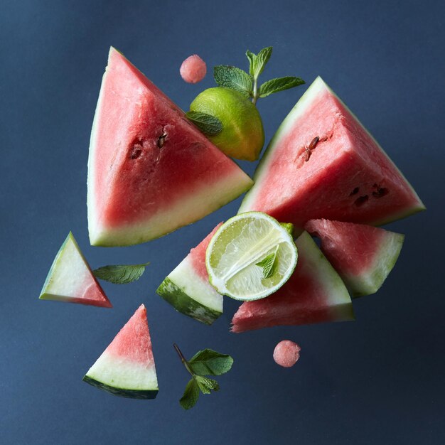 Geschnittene Wassermelonenscheiben isoliert auf schwarzer Oberfläche mit Limetten und Blättern