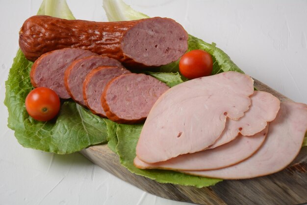 Geschnittene würzige geräucherte Rinder-/Schweinewurst und Puten-Pastrami-Scheiben. Mit Salatblatt und Basilikum, Kirschtomaten.