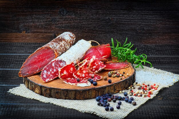 Geschnittene Wurst mit Gewürzen und einem Rosmarinzweig auf dunklem Holzhintergrund