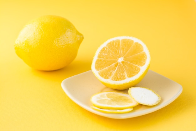 Geschnittene Zitrone auf einer Untertasse und eine ganze Zitrone daneben auf einem gelben Tisch.