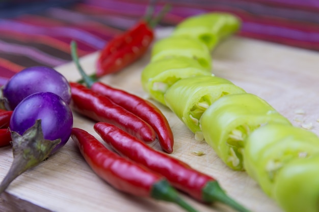 Geschnittener grüner Peper, roter Peper und Aubergine auf einem alten hölzernen Brett.