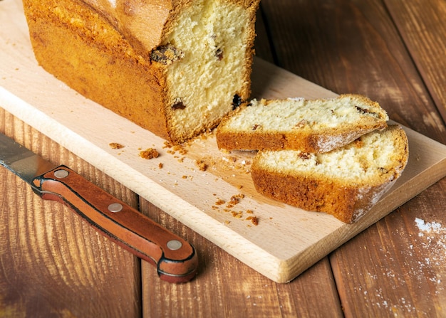 Geschnittener hausgemachter Cupcake mit Rosinen, bestreut mit Puderzucker auf einem Holzbrett und -messer. Hausmannskostidee für ein leckeres Frühstück