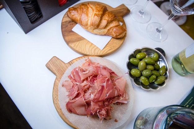 Geschnittener Jamon auf einem Holzbrett Gebäck Croissant und grüne Oliven