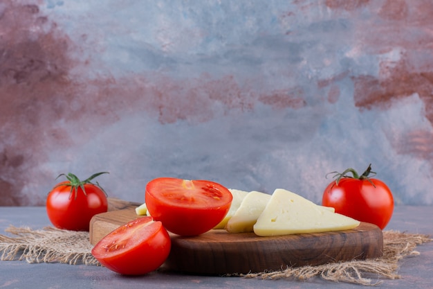 Geschnittener Käse und Tomaten auf einem Schneidebrett auf einer Leinenserviette auf der Marmoroberfläche