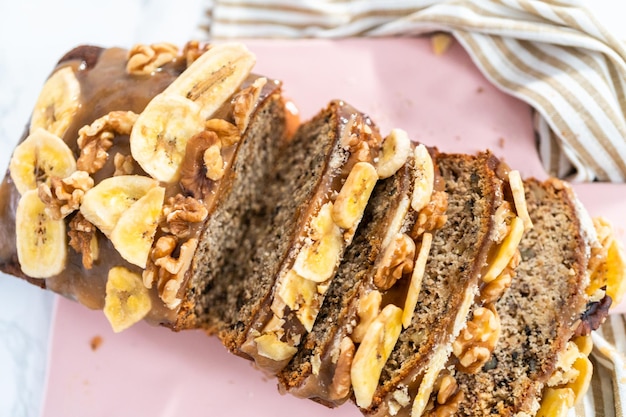 Geschnittener Laib Bananennussbrot beträufelte hausgemachtes Karamell auf einem rosa Schneidebrett.