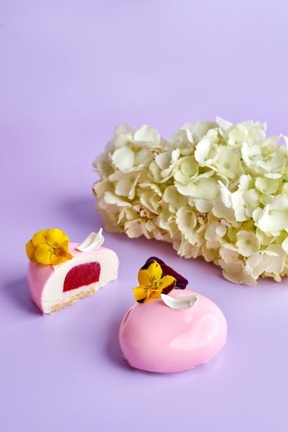 Geschnittener und ganzer Mousse-Kuchen auf rosa Hintergrund in einer Komposition mit Blumen