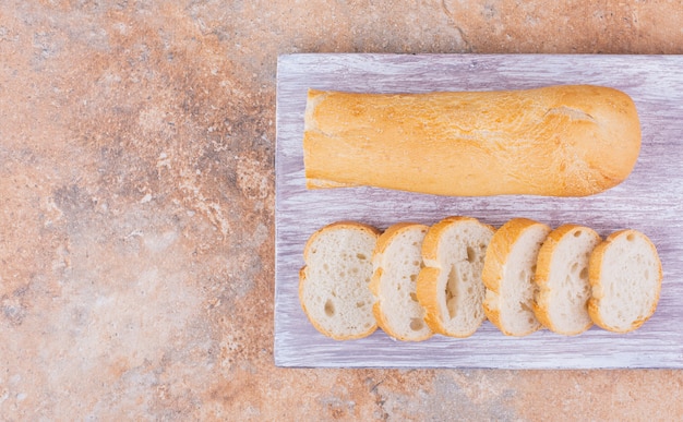 Foto geschnittenes baguette auf einem brett, auf dem marmorhintergrund.