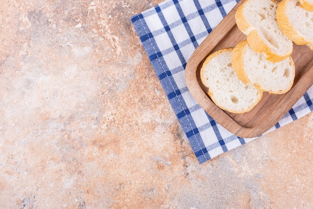 Geschnittenes Baguette auf einem Holzteller auf einem Handtuch auf dem Marmor.