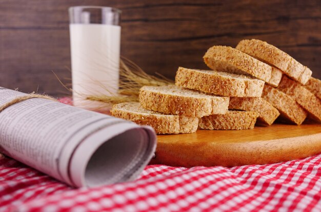 Geschnittenes Brot mit Milch und Zeitungspapier auf Tabelle