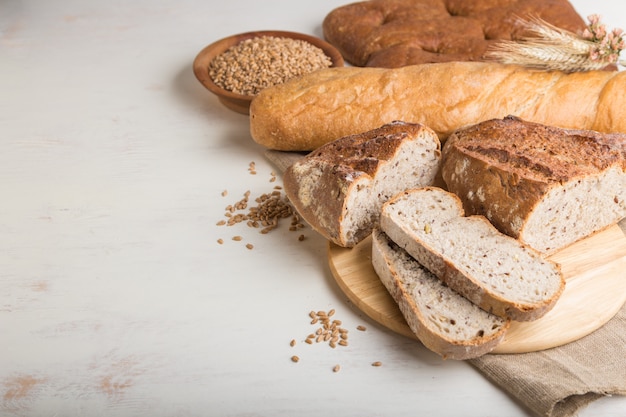 Geschnittenes Brot mit verschiedenen Arten von frisch gebackenem Brot auf einer weißen Holzoberfläche. Seitenansicht, Kopierraum.