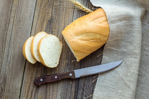 Geschnittenes Brot mit Weizenspitzen auf Holztischnahaufnahme.