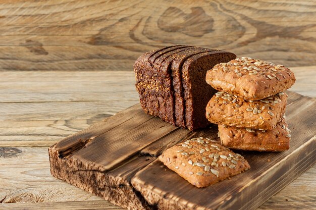 Geschnittenes frisch gebackenes Roggenbrot und mehrkörnige Scones auf Holzbrett auf rustikalem Hintergrund. Hausgemachte Bio-Lebensmittel.