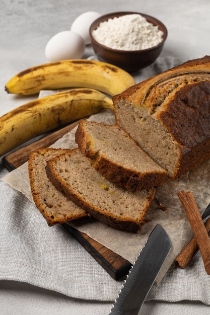 Geschnittenes frisches Bananenbrot mit Zutaten auf hellem Hintergrund