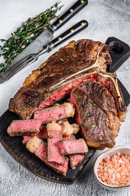 Geschnittenes gegrilltes T-Bone-Rindfleisch Steak auf einem hölzernen Schneidebrett auf weißem Tisch. Draufsicht.