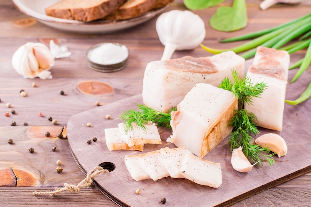 Geschnittenes gesalzenes Schweinefett mit Knoblauch und Dill auf einem Schneidebrett auf einem Holztisch.