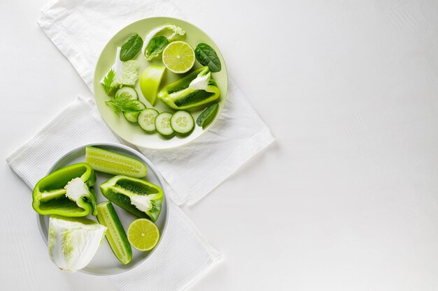 Geschnittenes grünes Gemüse und Obst auf Tellern. Grüne Diätkost auf weißem Hintergrund. Gesundes und vegetarisches Essen. Ansicht von oben