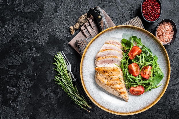 Geschnittenes Hähnchenbrustfiletsteak mit grünem Salat in einem Teller Schwarzer Hintergrund Draufsicht Kopierbereich