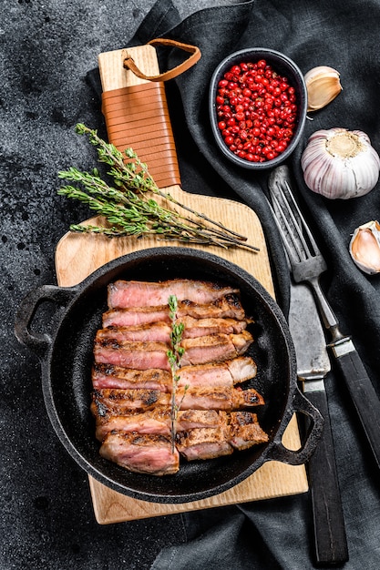 Geschnittenes Schweinekotelettsteak auf einem Knochen mit Gewürzen und Kräutern. Schwarzer Hintergrund.