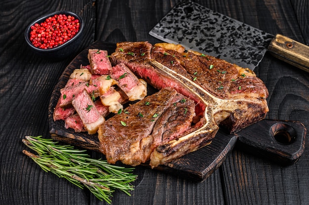 Geschnittenes und gebratenes T-Bone- oder Porterhouse-Rindfleisch Steak für Steakhouse-Menü. Schwarzer hölzerner Hintergrund. Ansicht von oben.