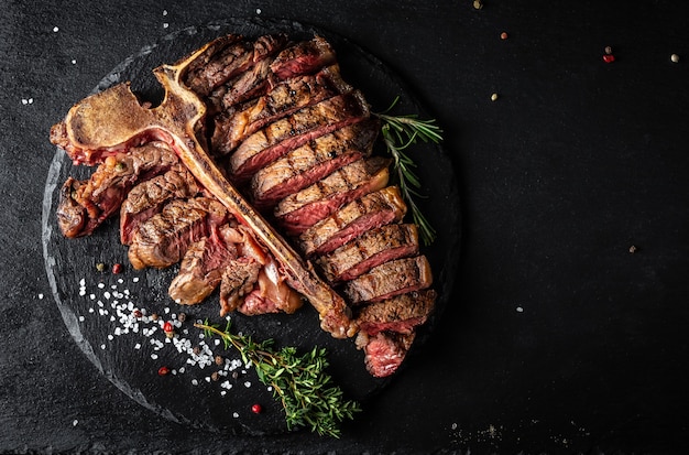 Geschnittenes und geröstetes T-Bone- oder Porterhouse-Rinderfleischsteak für Steakhouse-Menü auf schwarzer Oberfläche