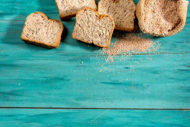 Geschnittenes Vollbrot und kleine Tasche mit Vollkornmehl auf strukturiertem blauem Holzraum für Text, Draufsicht.