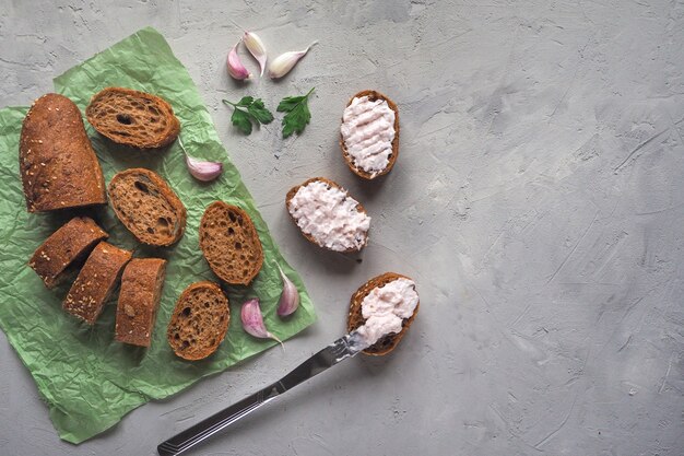 Geschnittenes Vollkornbaguette mit Knoblauchcreme auf einem grauen Zementtisch. Kopierbereich der Draufsicht