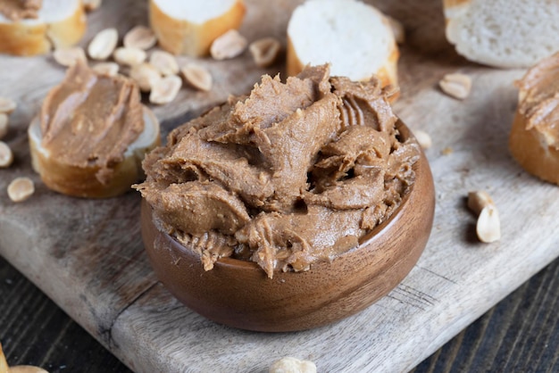 Geschnittenes Weißbrot mit gebutterter Erdnussbutter mit zerdrückten Erdnussstückchen auf einem Holzbrett in der Küche