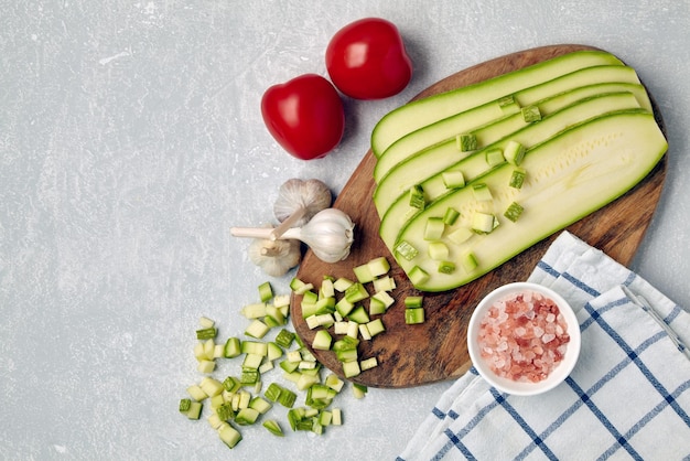 Geschnittenes Zucchini-Gemüse auf einem Holzschneidebrett Tomaten Knoblauch rosa Salz und Serviette auf einem Betontisch Draufsicht mit Kopierbereich Flach liegend