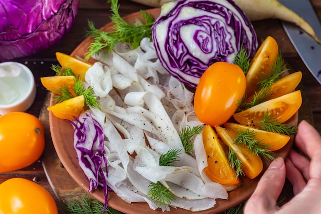 Geschredderter Rotkohl-Rettich und gelbe Tomaten mit Dill in Tonschale auf schwarzem Hintergrund