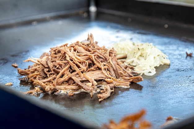 Geschreddertes Fleisch, das auf einem Teller mit Zwiebeln und Butter für Brotsandwich röstet. Straßenessen.