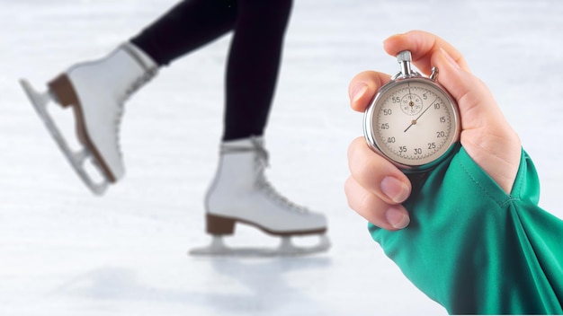 Geschwindigkeitsmessung auf Schlittschuhen mit einer Stoppuhr. Hand mit einer Stoppuhr auf dem Hintergrund der Beine eines Mannes, der auf einer Eisbahn Schlittschuh läuft