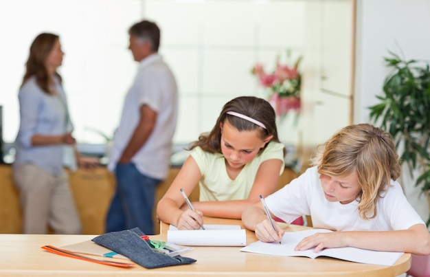 Geschwister, die Hausaufgaben mit ihren Eltern hinter ihnen tun