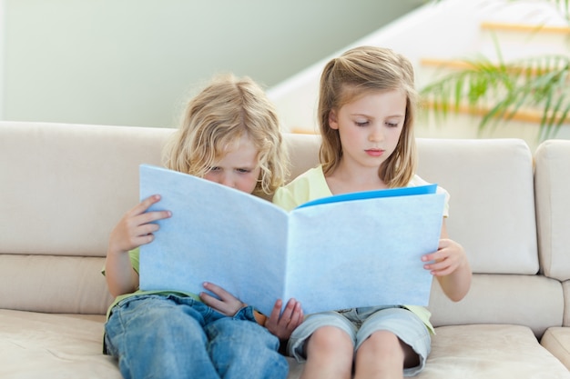 Foto geschwister, die zeitschrift auf dem sofa lesen