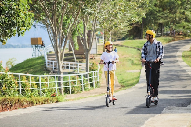 Geschwister im Urlaub haben Spaß daran, mit dem Elektroroller durch den Straßenpark zu fahren. Jugend Freizeit Famil