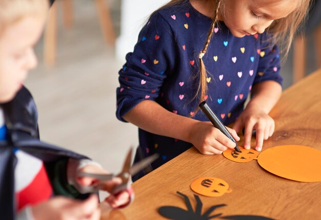 Foto geschwister machen halloween-dekoration auf dem tisch zu hause