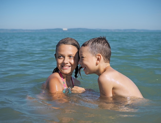 Geschwister schwimmen im Meer vor klarem Himmel