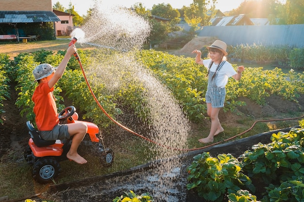 Geschwisterkinder toben in den sommerferien im hinterhof im garten planschend mit einem wasserschlauch