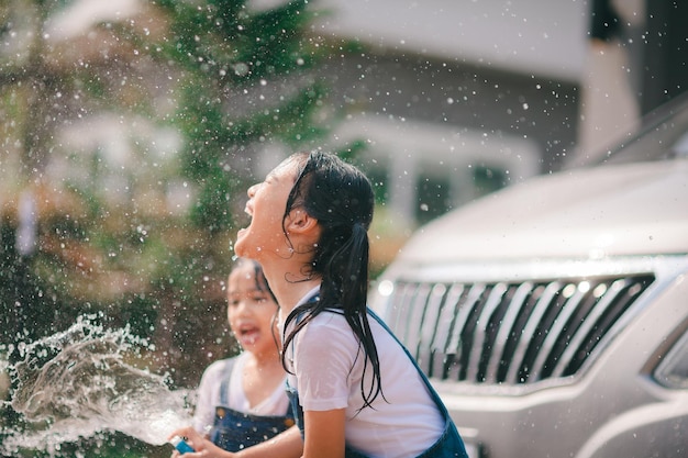 Geschwisterliche asiatische Mädchen waschen ihre Autos und spielen an einem heißen Sommertag drinnen