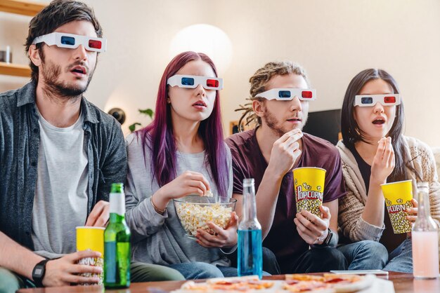 Gesellschaft junger Freunde, die Popcorn essen und Filme in 3D-Brillen auf der Couch sitzen