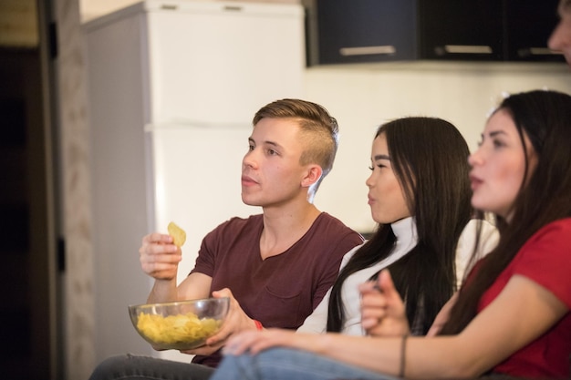 Gesellschaft junger Freunde, die Zeit miteinander verbringen, fernsehen und Popcorn und Chips essen