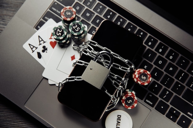Gesetz und Regeln für Online-Glücksspielkonzept, Smartphone mit Vorhängeschloss und Spielkarten auf Laptop-Tastatur.