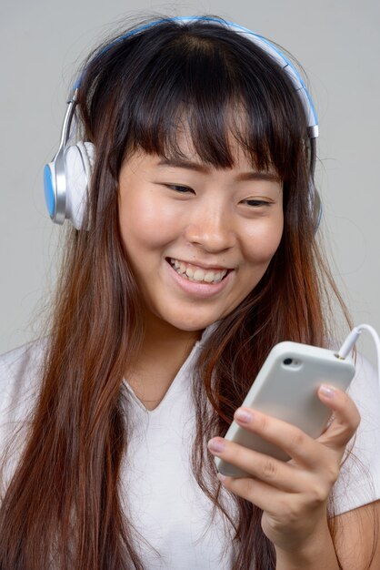 Gesicht der glücklichen jungen asiatischen Frau, die Telefon beim Musikhören verwendet