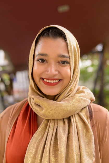 Gesicht der glücklichen jungen schönen indischen muslimischen Frau, die in der Stadt mit Natur lächelt
