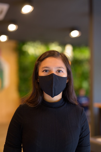 Gesicht der jungen asiatischen Geschäftsfrau, die Maske zum Schutz vor Ausbruch des Koronavirus innerhalb des Coffeeshops trägt