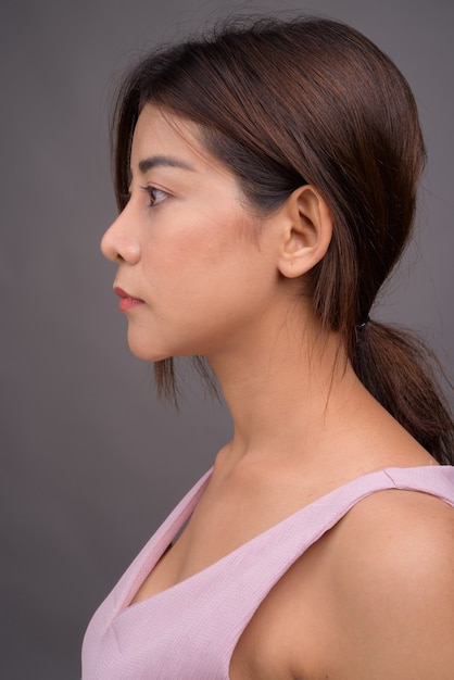 Gesicht der jungen schönen asiatischen Frau gegen graue Wand