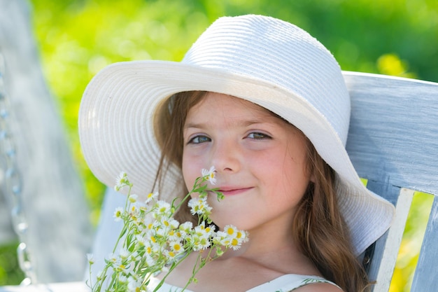 Gesicht des Frühlingskindes Schließen Sie herauf Porträt eines kleinen blonden Kindmädchens mit Frühlingsblume Lustige Kinder im Hinterhof Kinder schließen Gesicht auf Blütehintergrund Kindermädchen spielen in Frühlingsblumen