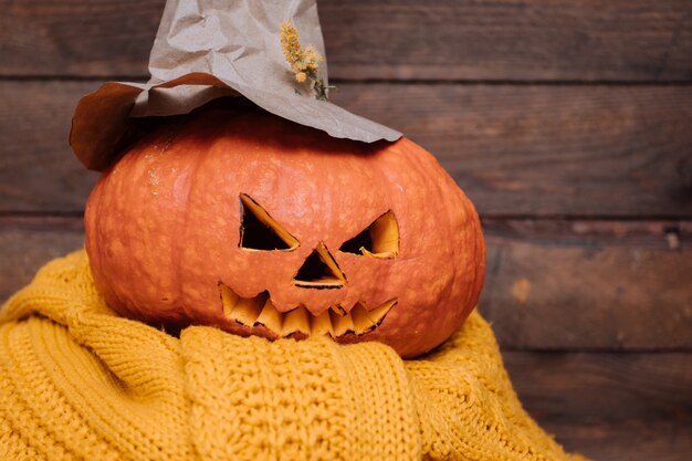 Gesicht des geschnitzten Halloween-Kürbisses mit Hexenhut auf gelbem Pullover.