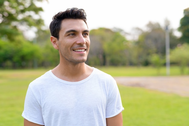 Gesicht des glücklichen jungen gutaussehenden hispanischen Mannes, der am Park denkt