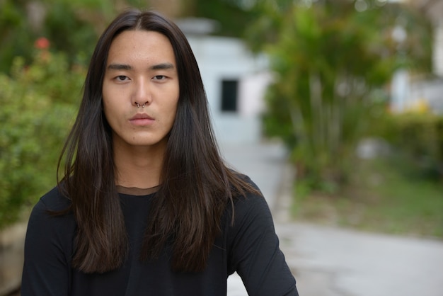 Gesicht des jungen asiatischen Mannes mit den langen Haaren am Park