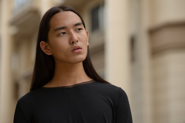 Gesicht des jungen asiatischen Mannes mit den langen Haaren, die in der Stadt denken